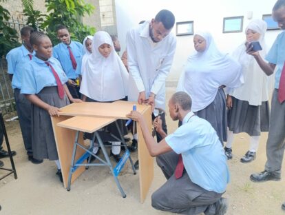 Concentration all round from the students as the teacher supervises the use of a hammer to help build the library bookcase.